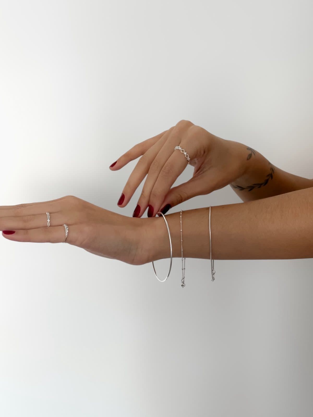 Mãos com anéis finos e duas pulseiras de prata sobre fundo claro